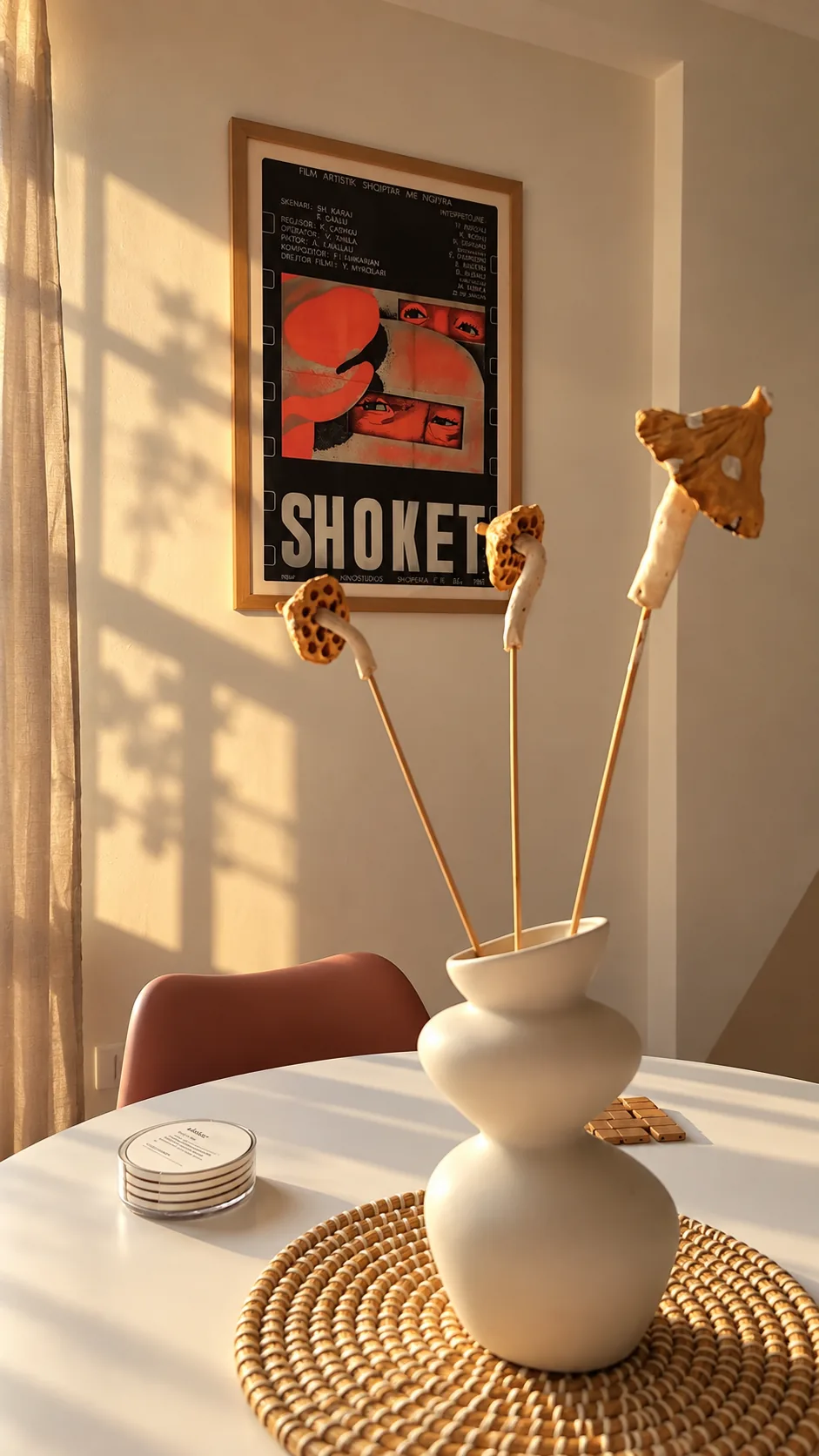 White vases on the dining table with a Shokët film poster behind.