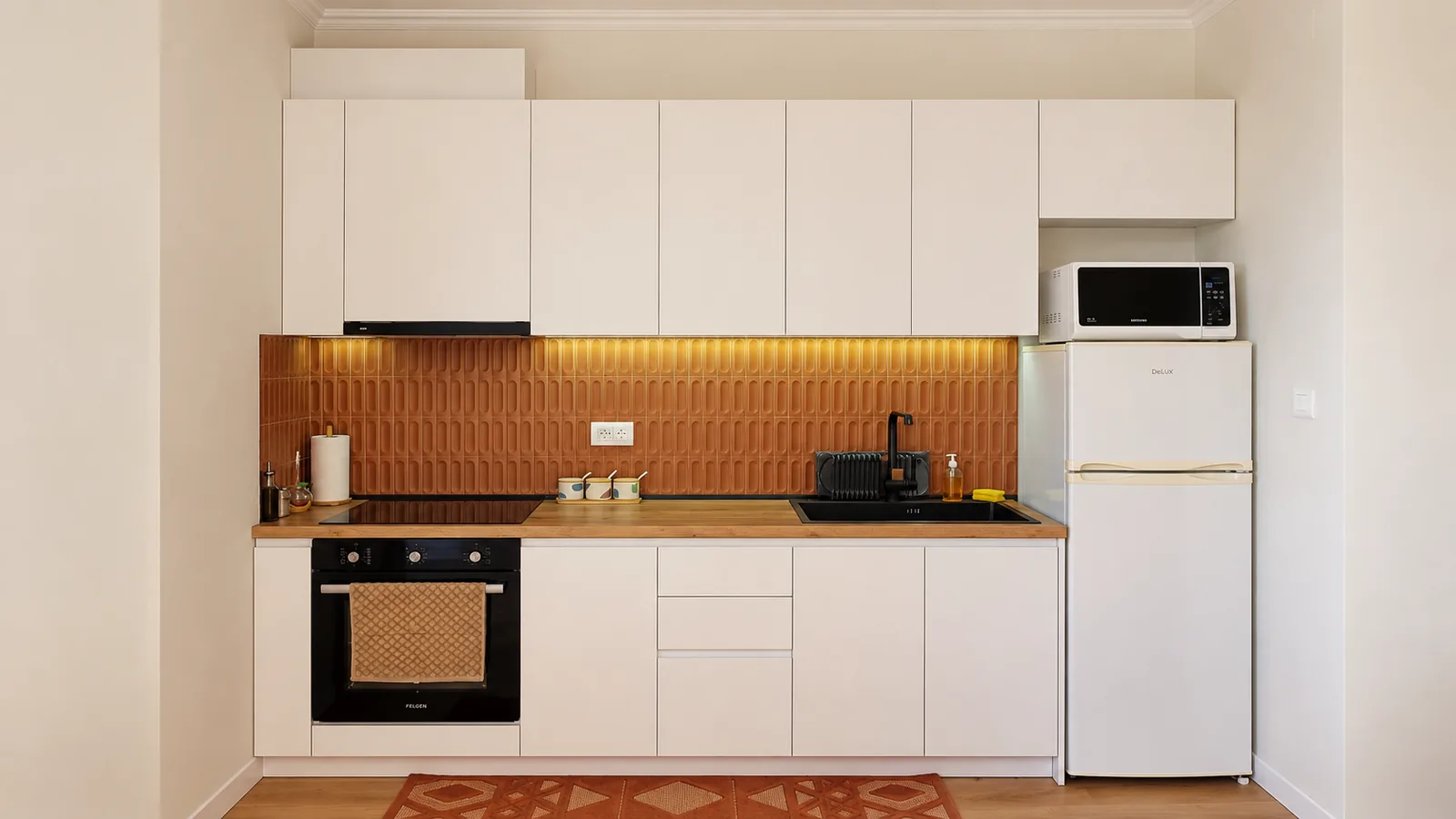 White kitchen cabinets with oven, hob, microwave and orange-tiled backsplash.