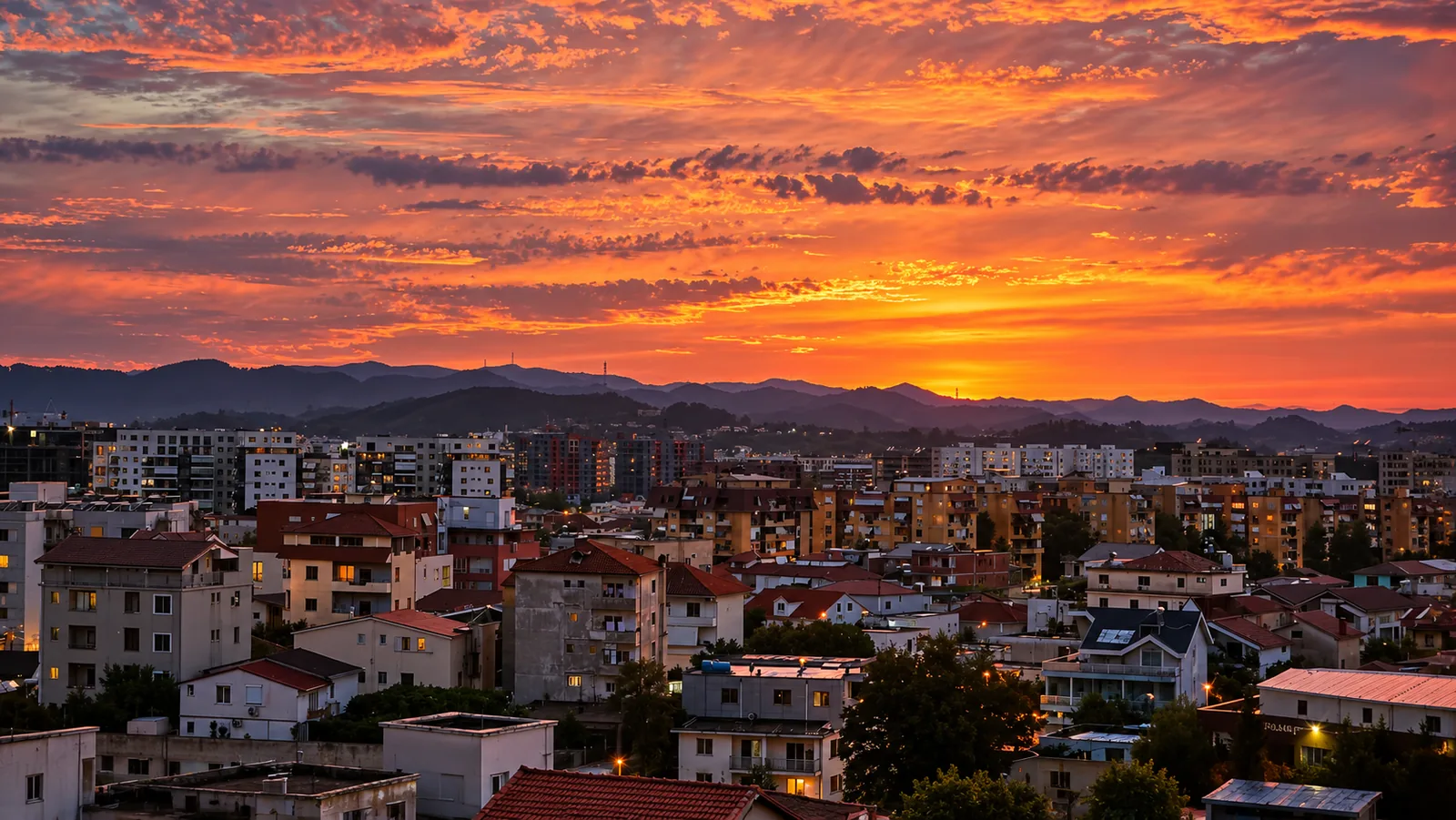 Tirana rooftops and distant mountains beneath orange and pink sunset clouds.
