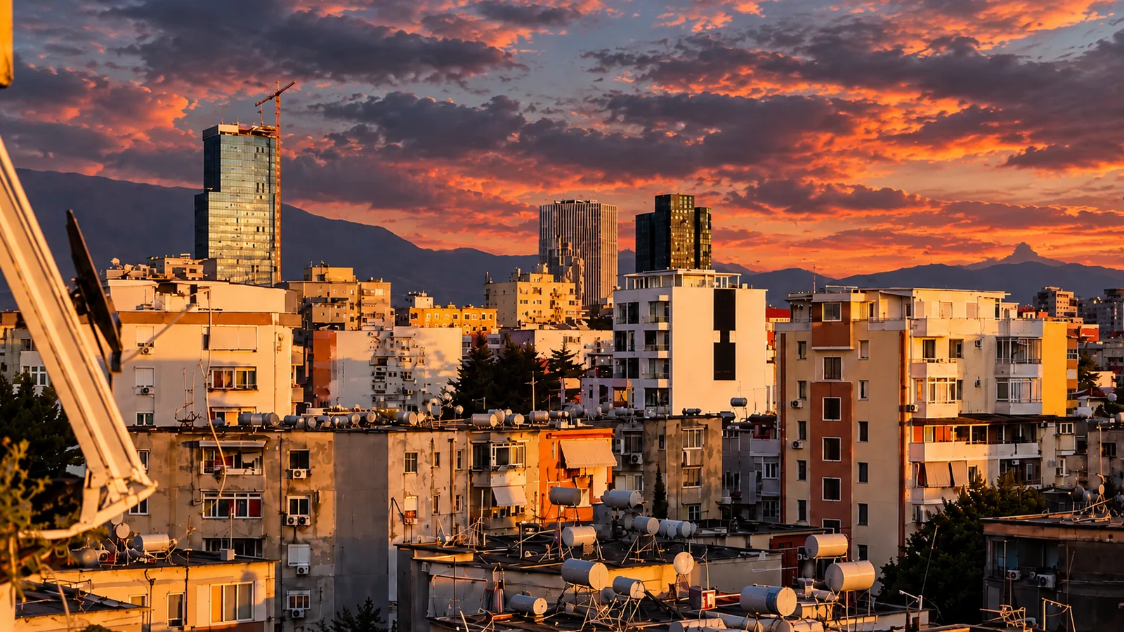 View from the apartment window across Tirana buildings beneath a colourful evening sky.