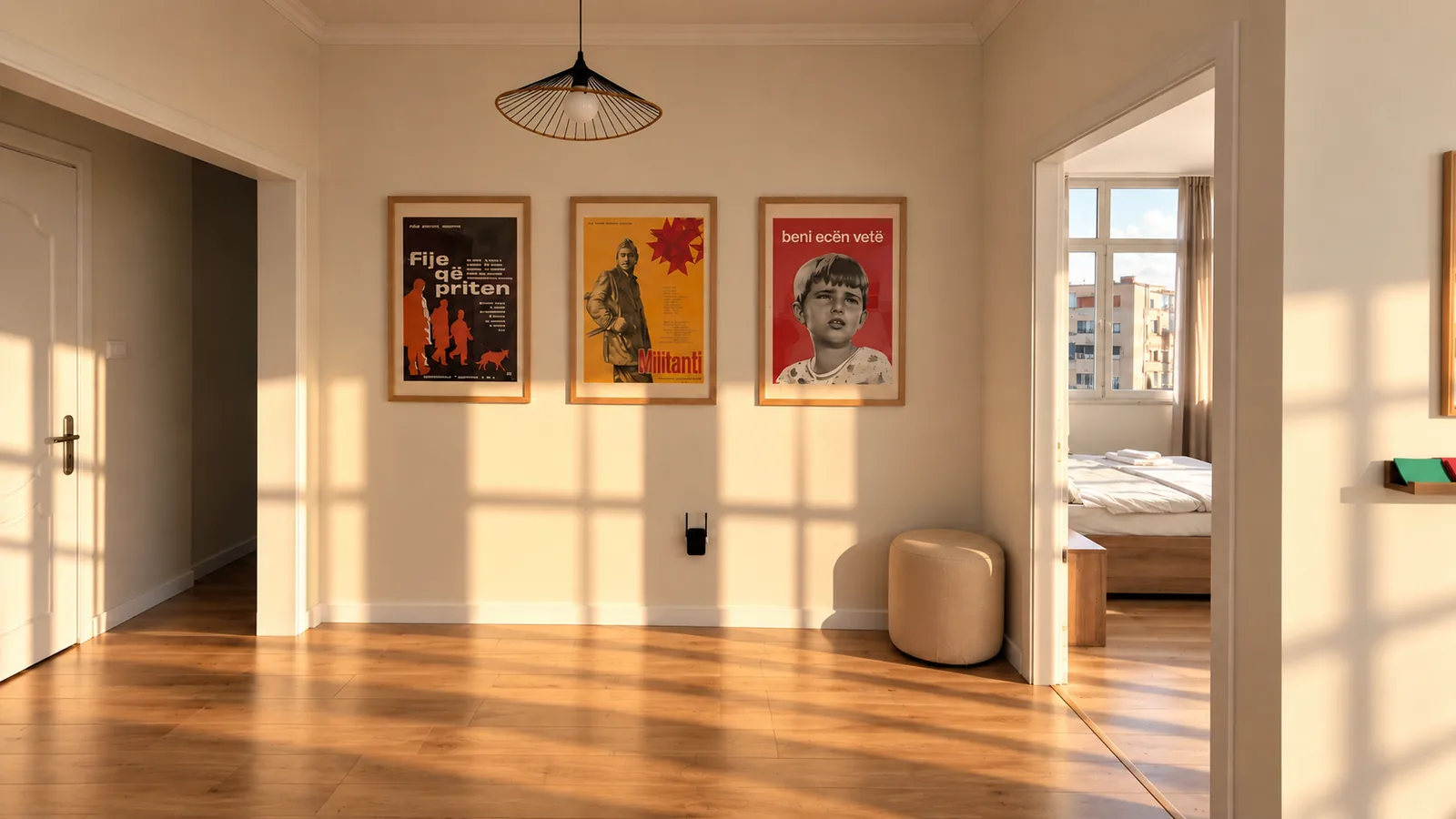 Sunlit hallway with three framed Albanian film posters and an open bedroom doorway.